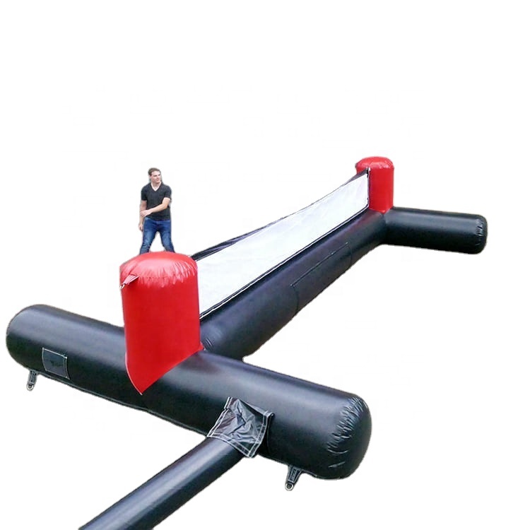 A person stands on a large inflatable structure shaped like a foosball table, featuring black and red sections with a central white area.