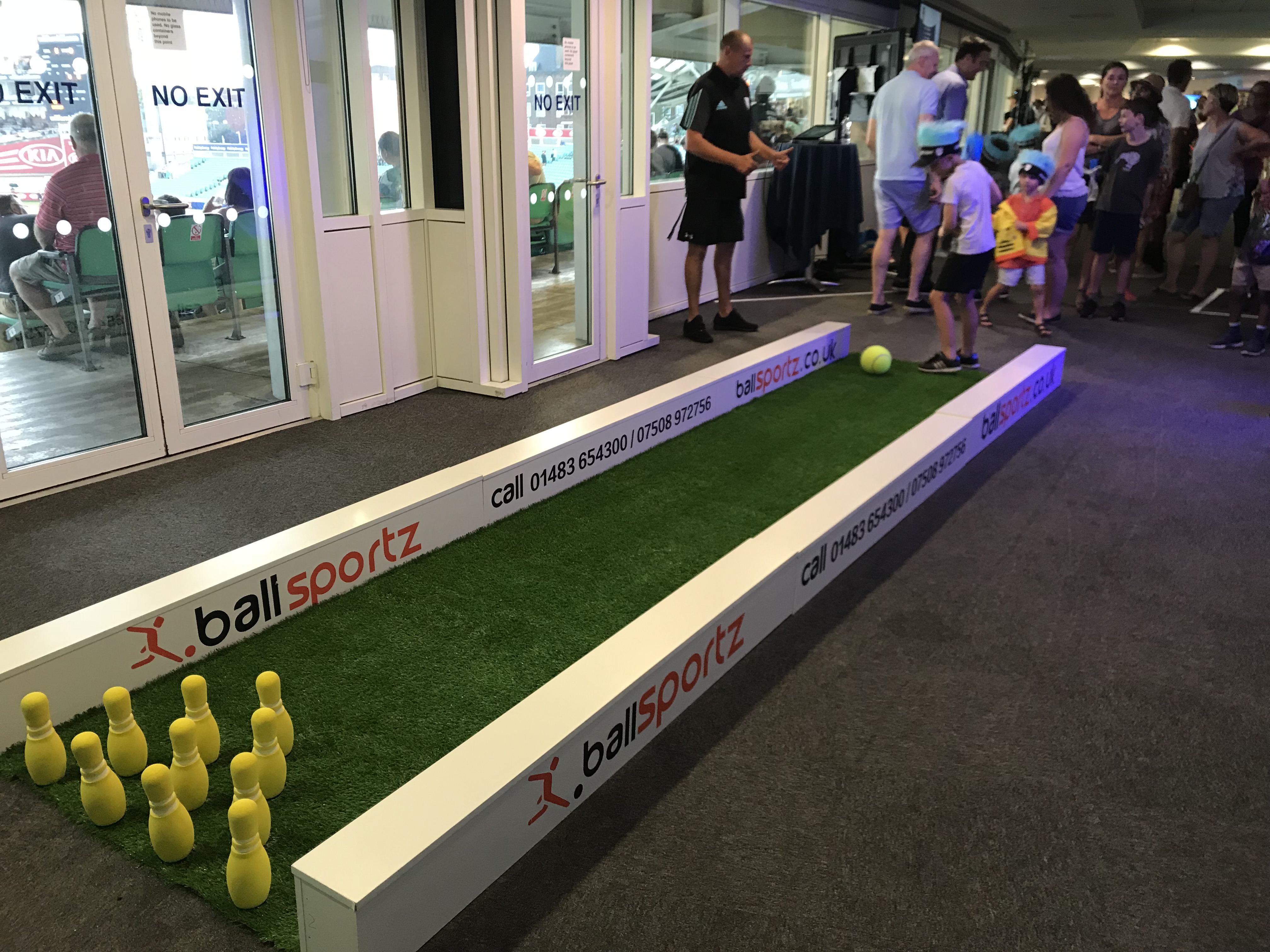 A child prepares to kick a soccer ball at a set of yellow pins on an indoor mini soccer bowling lane.