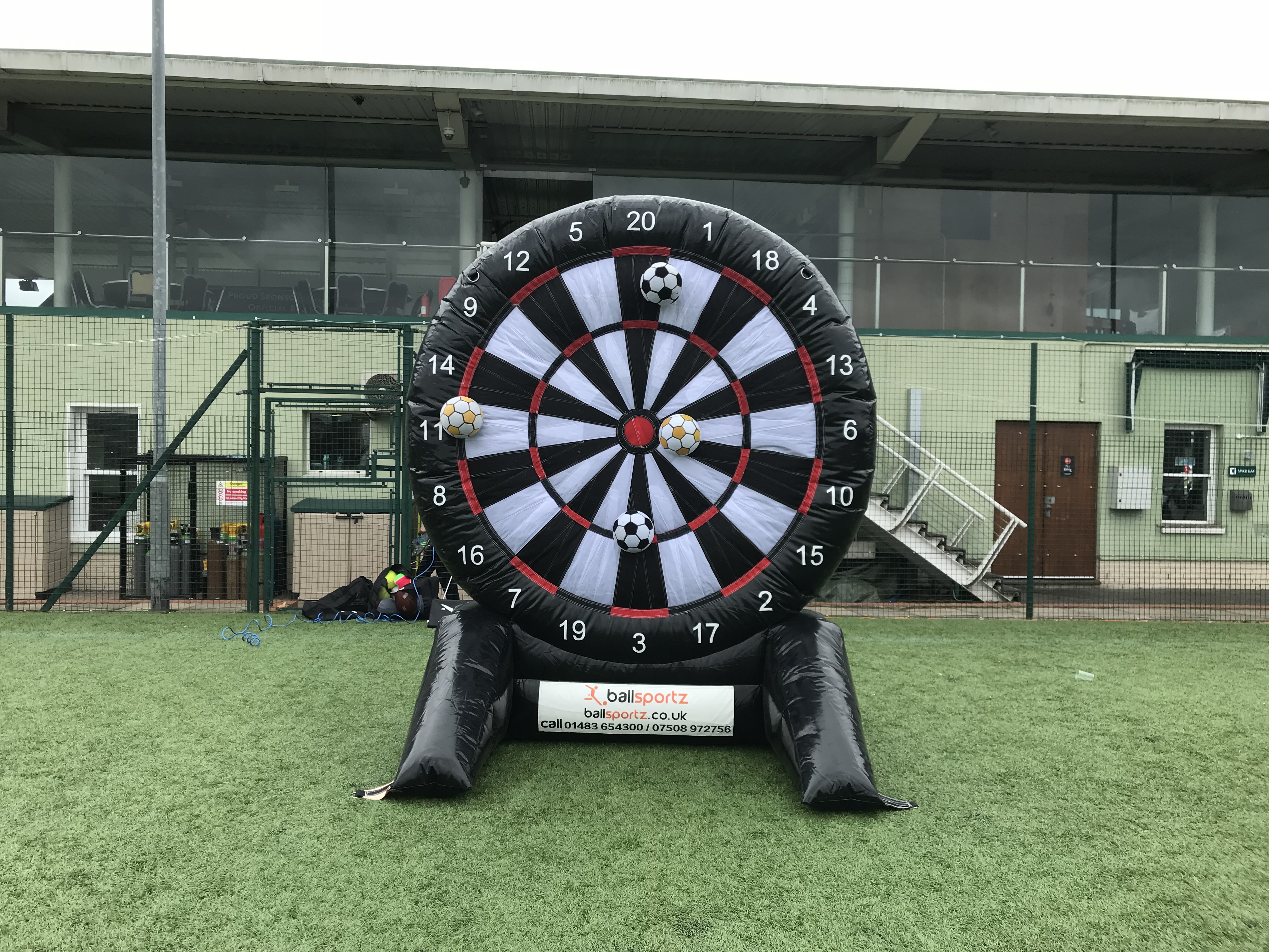 Inflatable dartboard game with soccer balls, set up on a sports field.