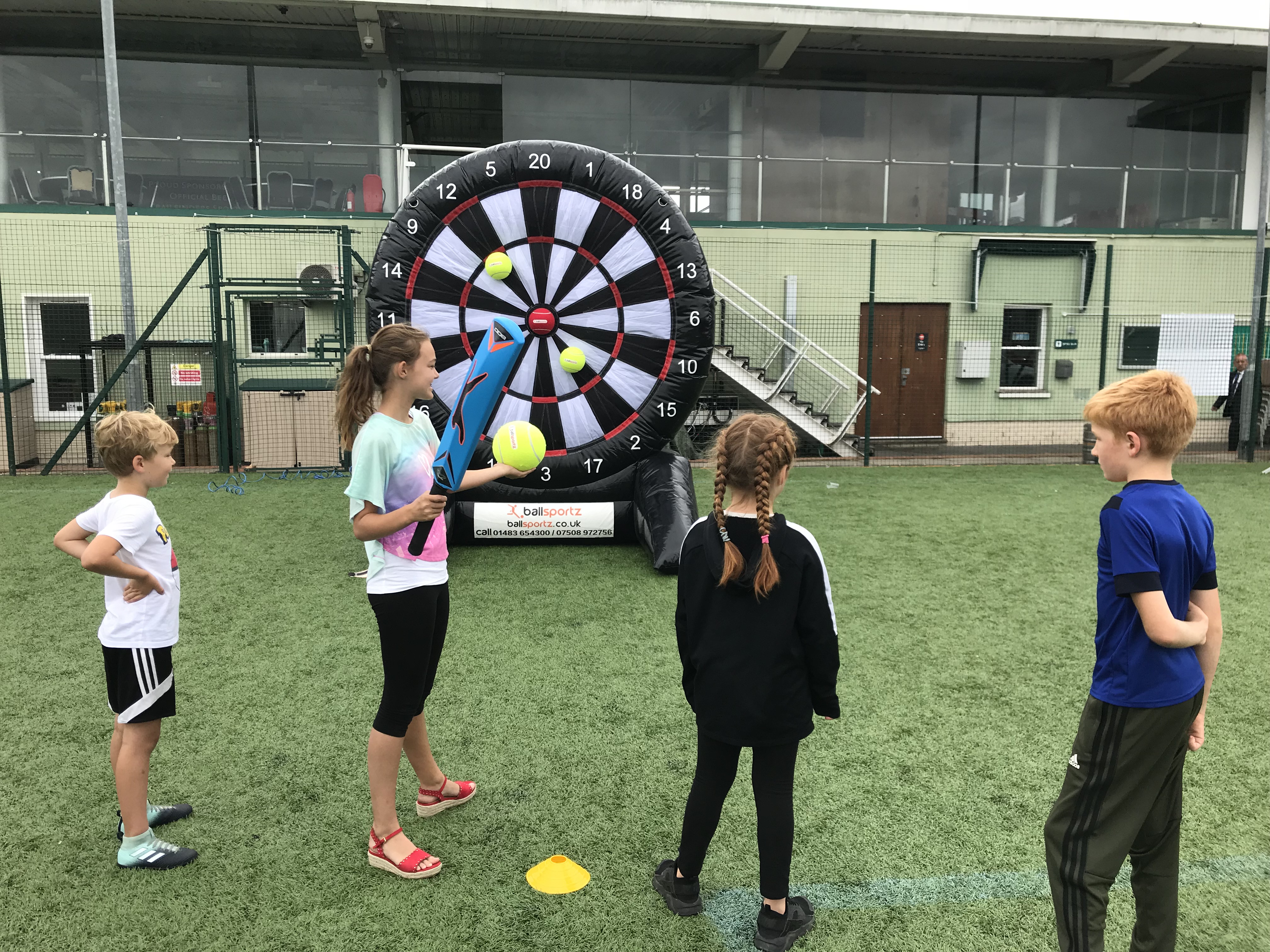 Four children play a game of inflatable soccer darts on a grassy field.