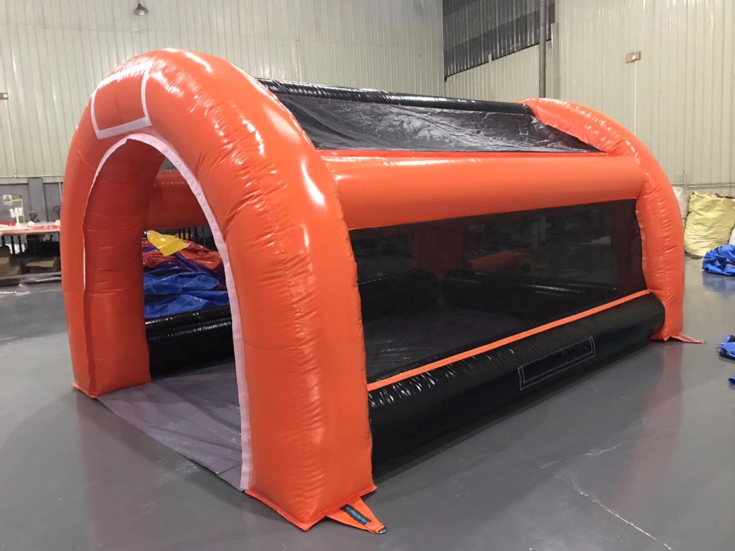 Inflatable orange and black sports cage with a mesh side in an indoor setting.