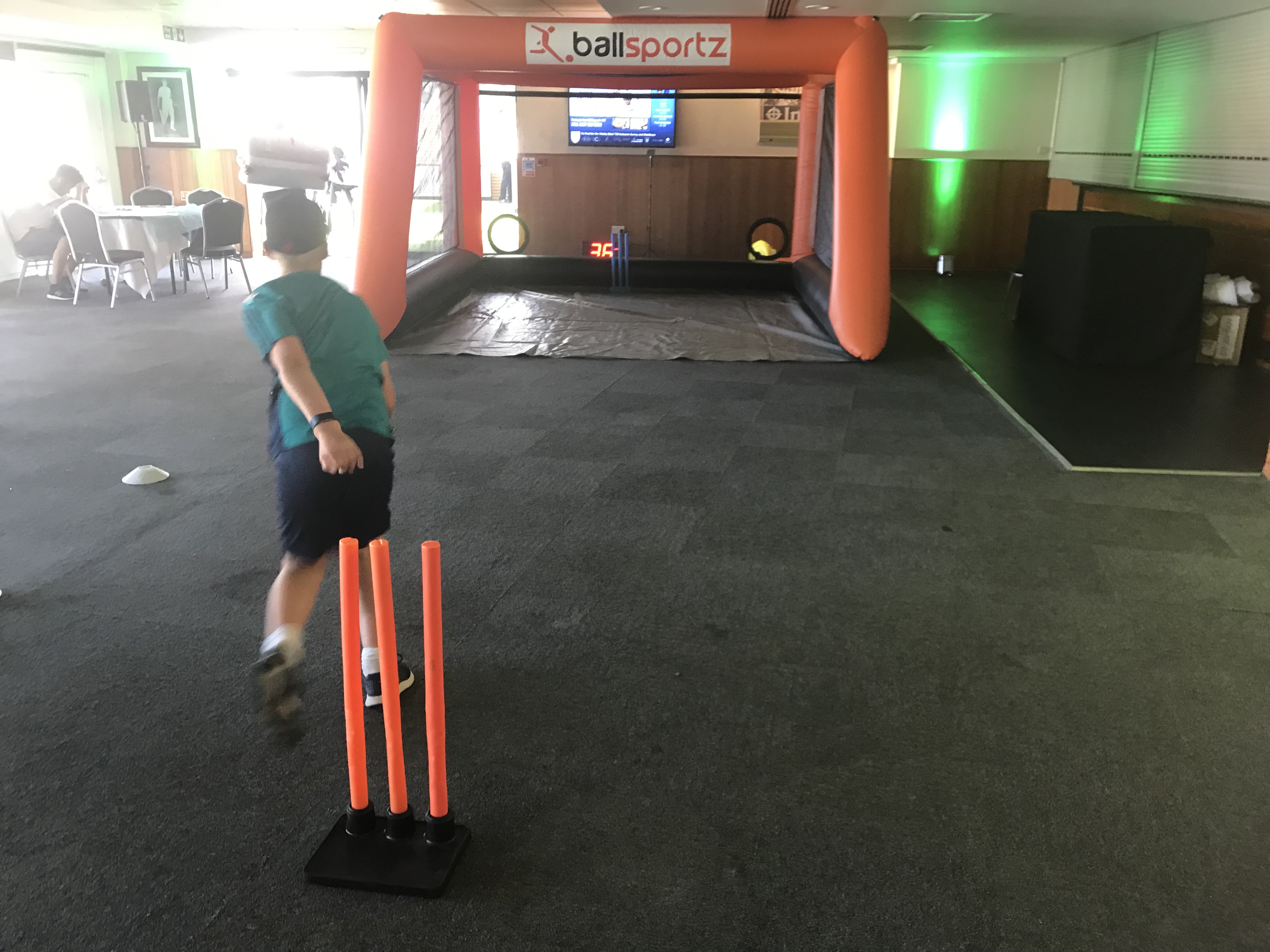 A person playing an indoor cricket game, aiming at an inflatable target with orange stumps in the foreground.