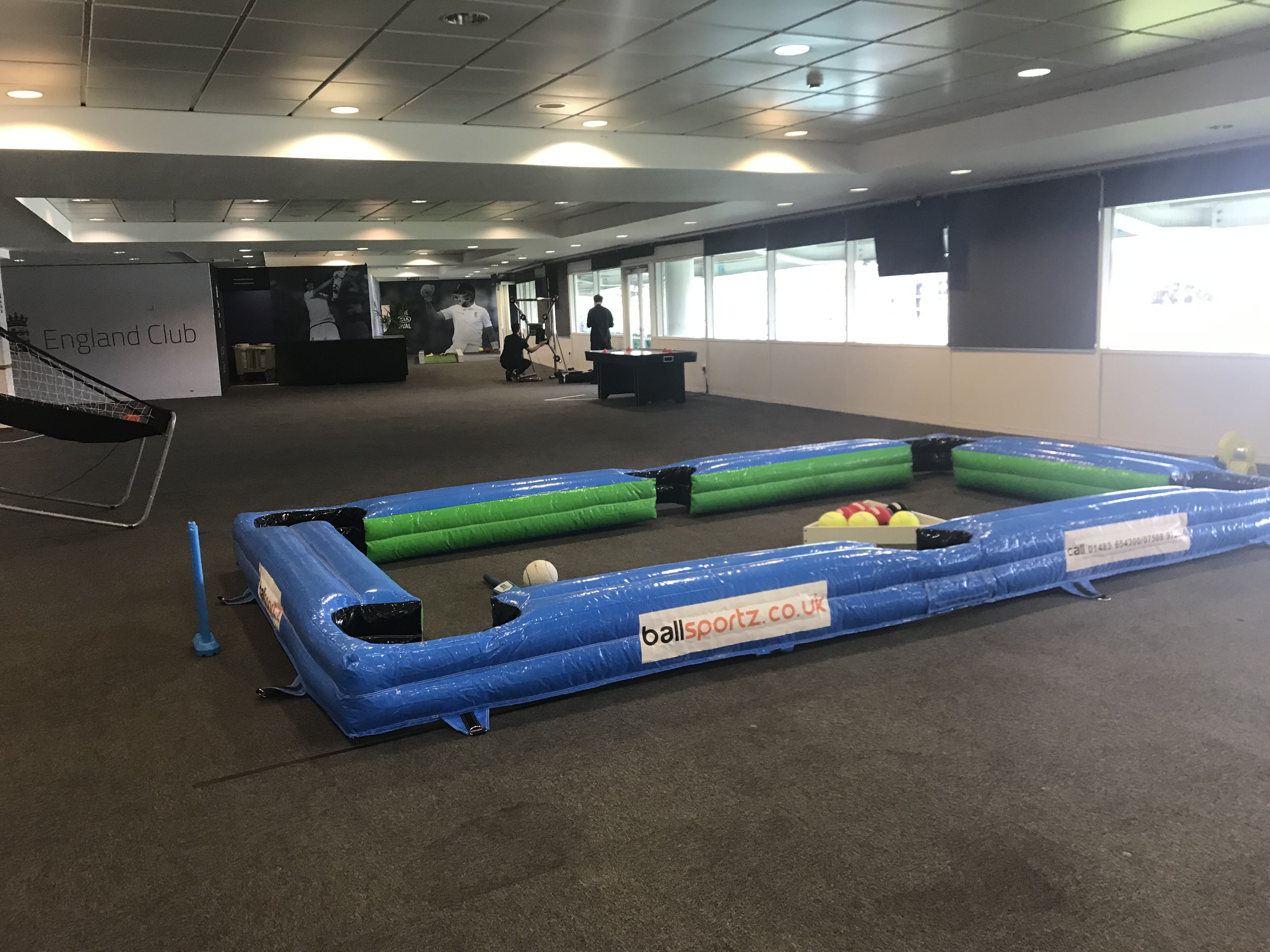 An inflatable pool table set up indoors with soccer balls placed on it.