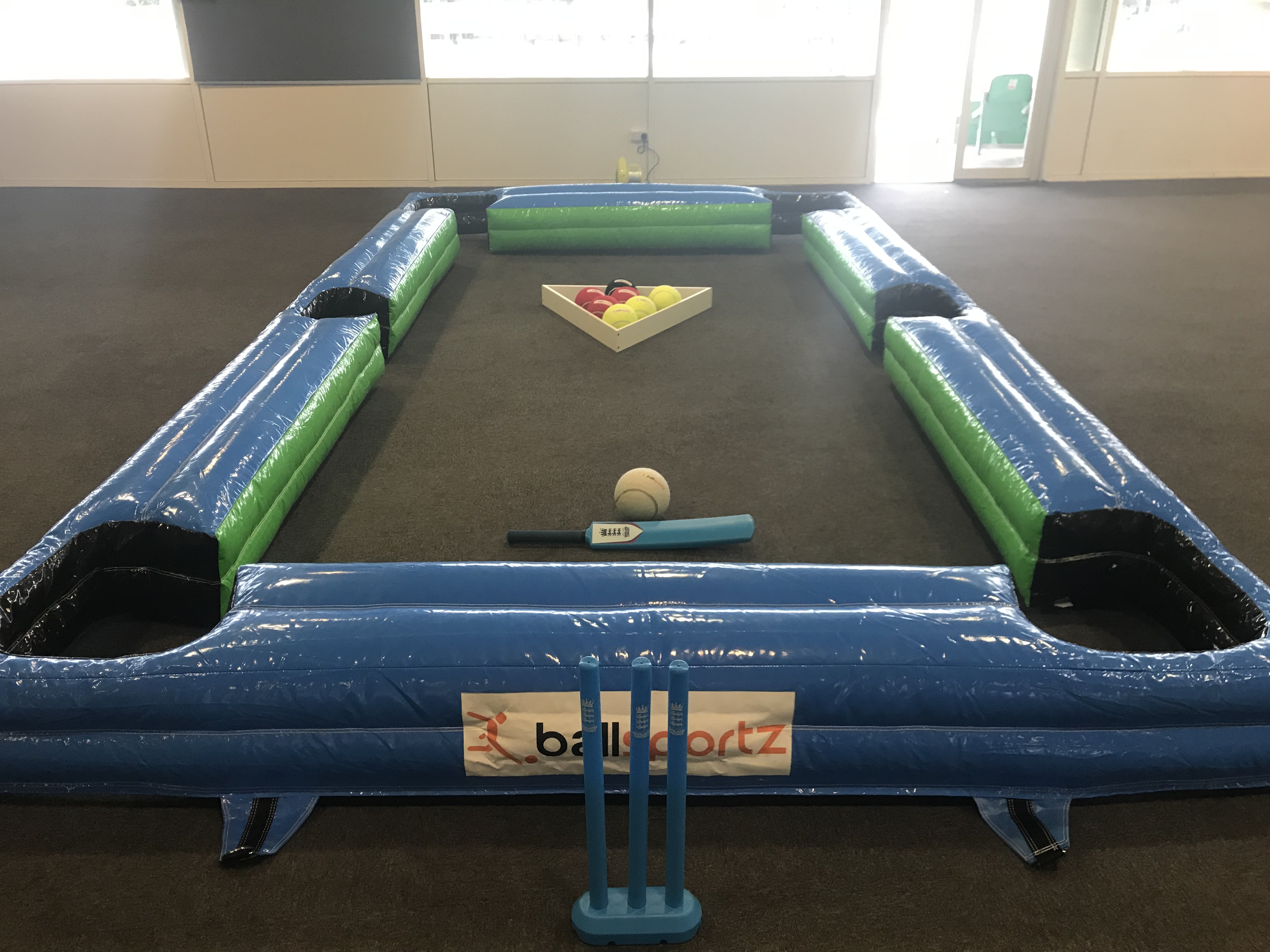 Inflatable snooker table setup with cricket twist, featuring a cricket bat, ball, and blue stumps, surrounded by green and blue cushions.