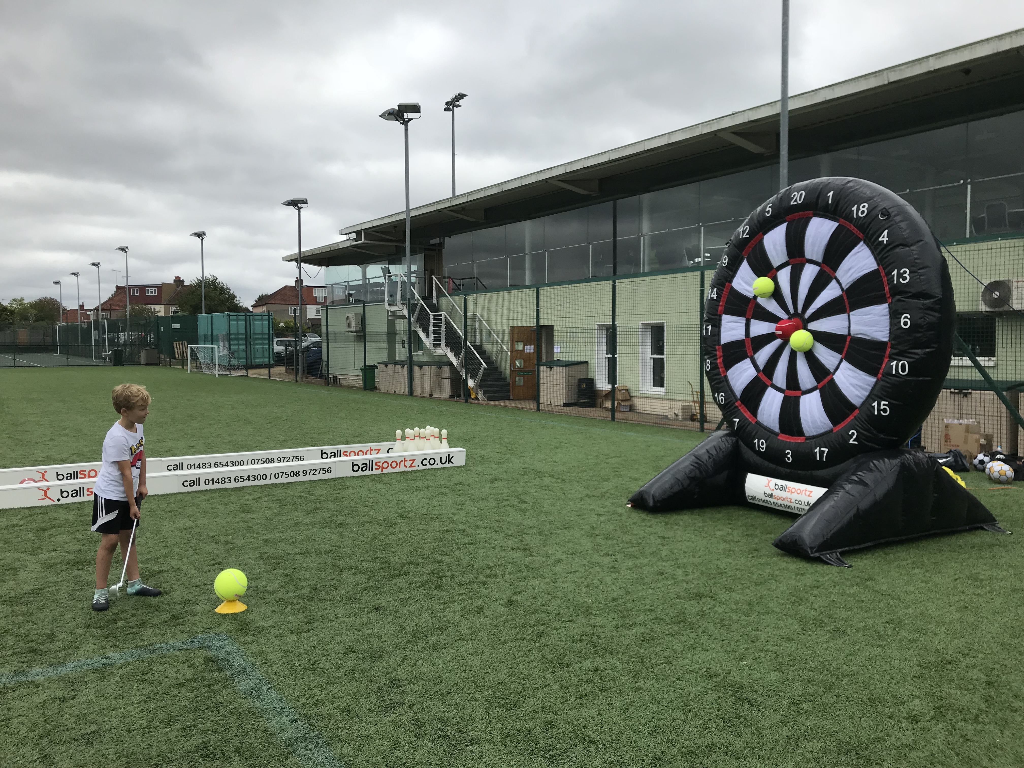A child aims a ball at an inflatable dartboard on a sports field.