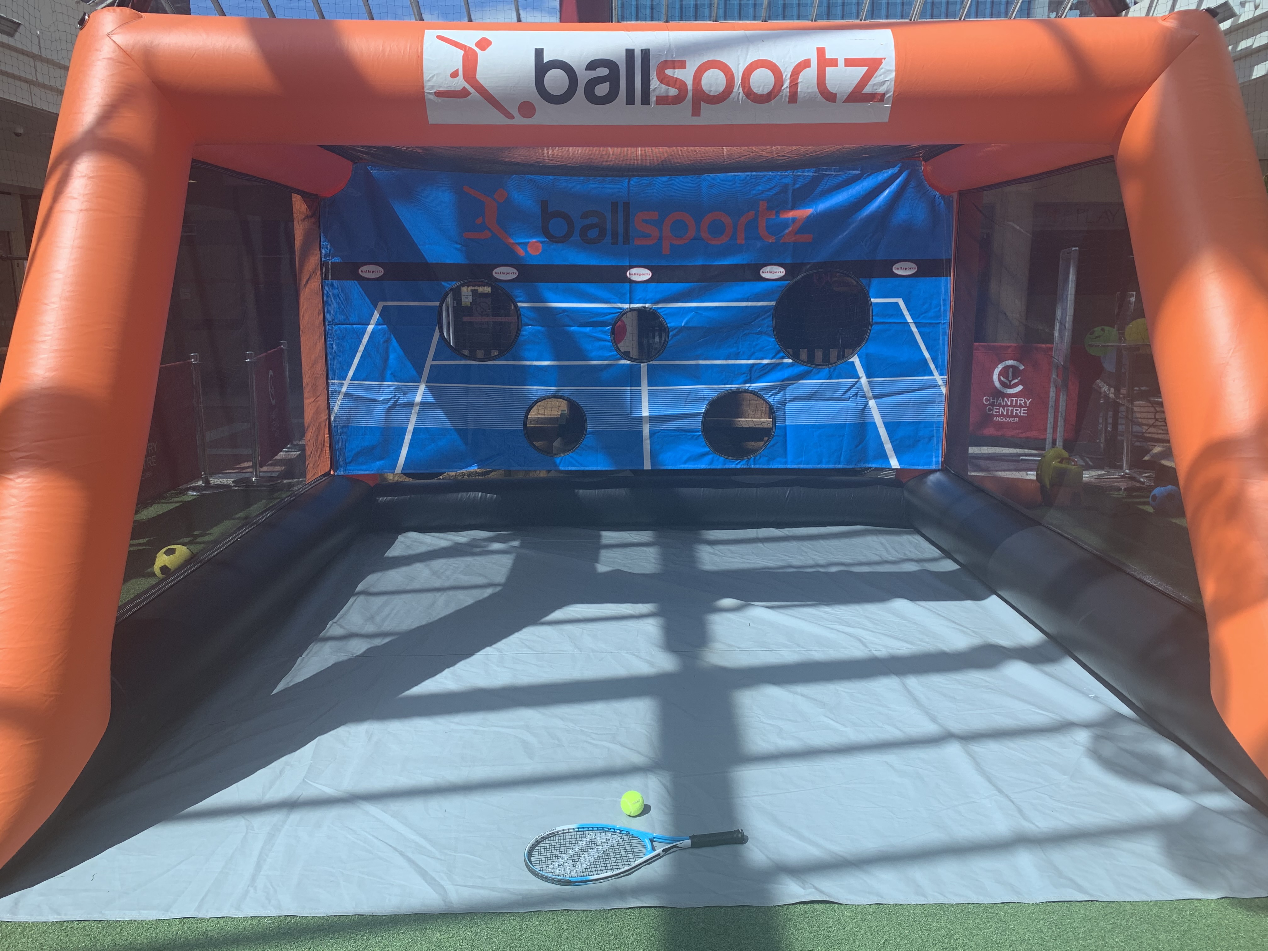 An inflatable ball sport booth with a target net, tennis racket, and ball on the ground inside.