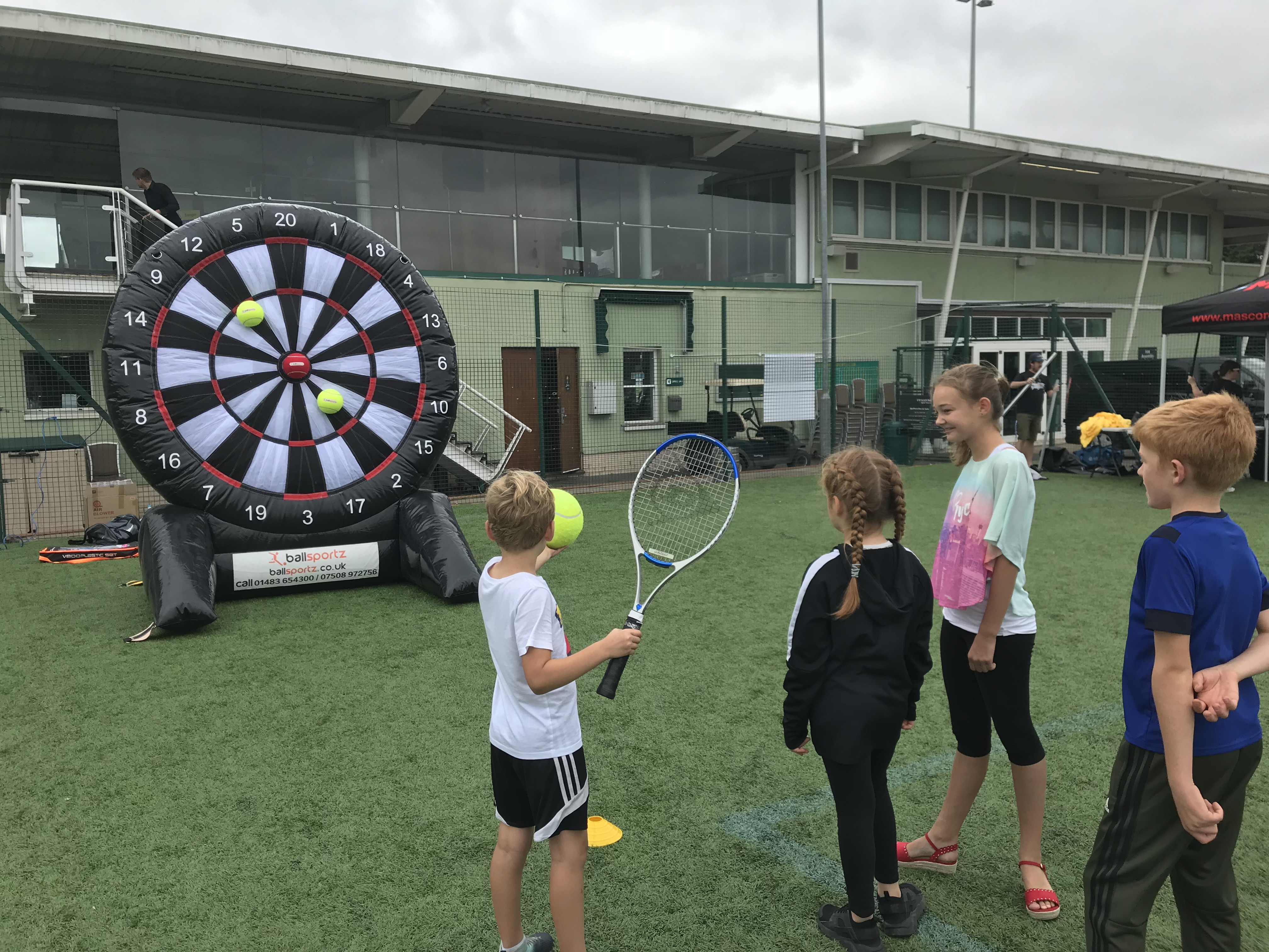 Children playing a tennis-themed dart game on a sports field.