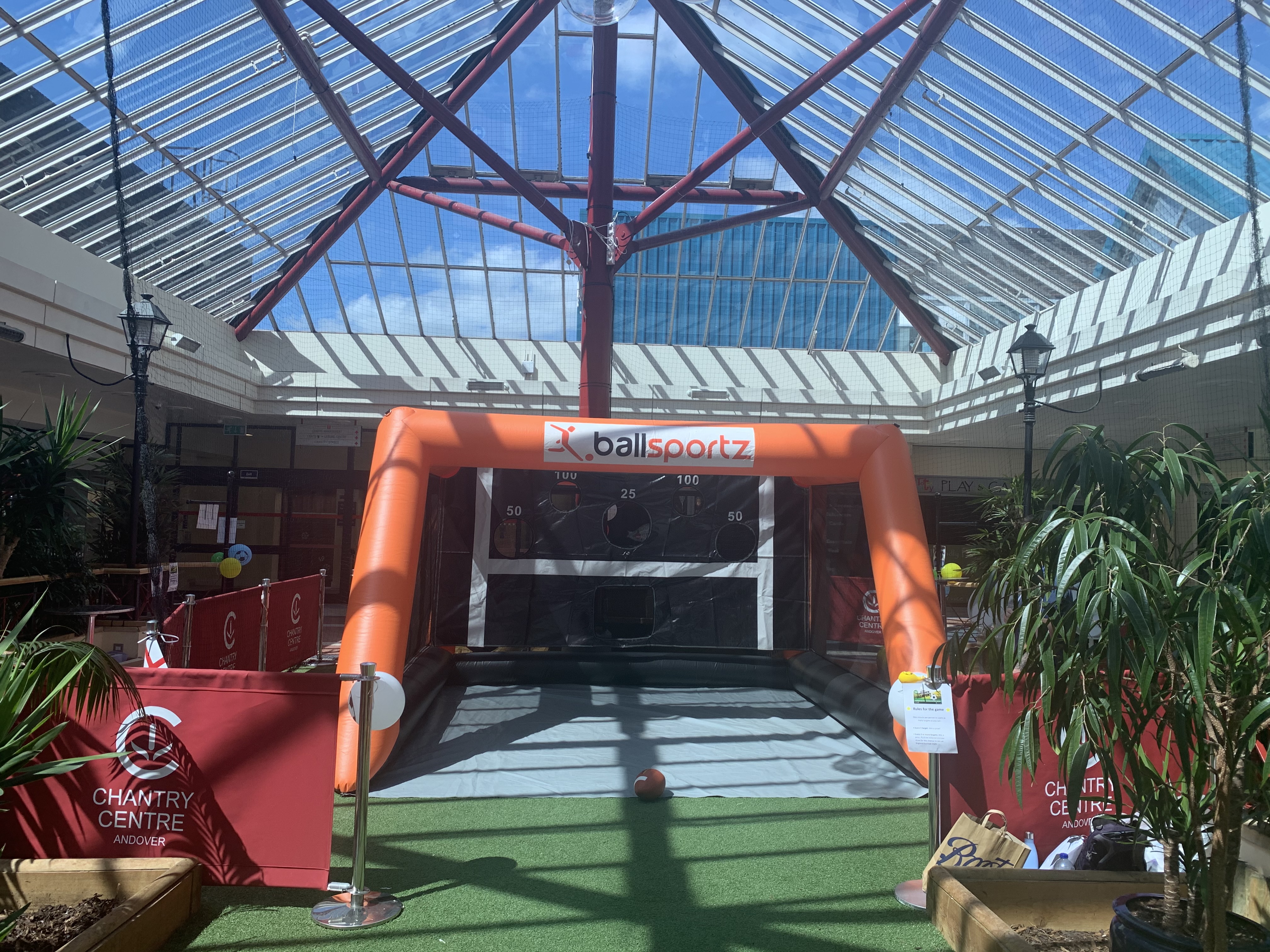 An inflatable soccer goal game setup inside a glass-roofed shopping center.
