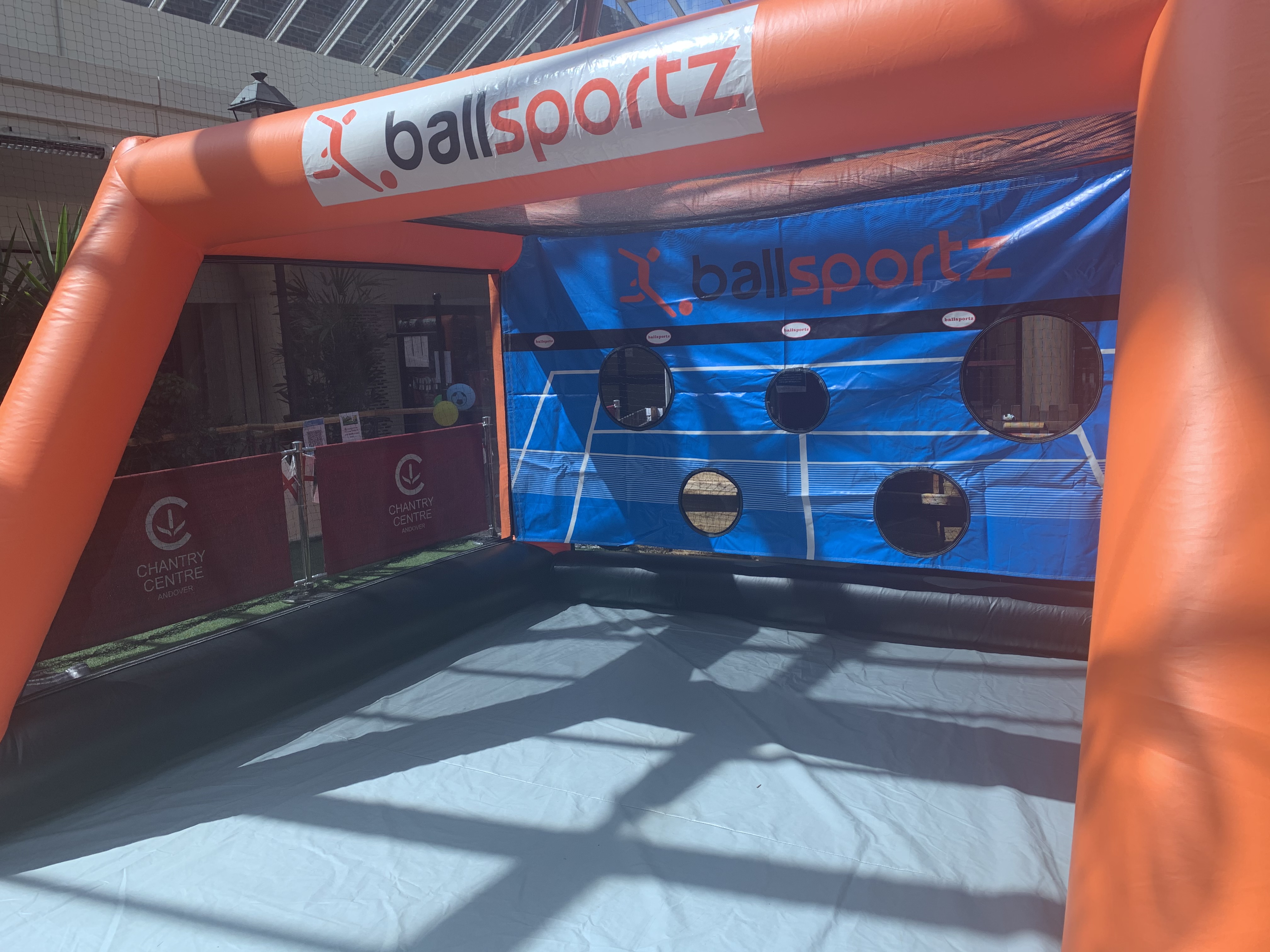 Inflatable ballsportz game setup with target holes, located indoors under a glass roof at Chantry Centre.