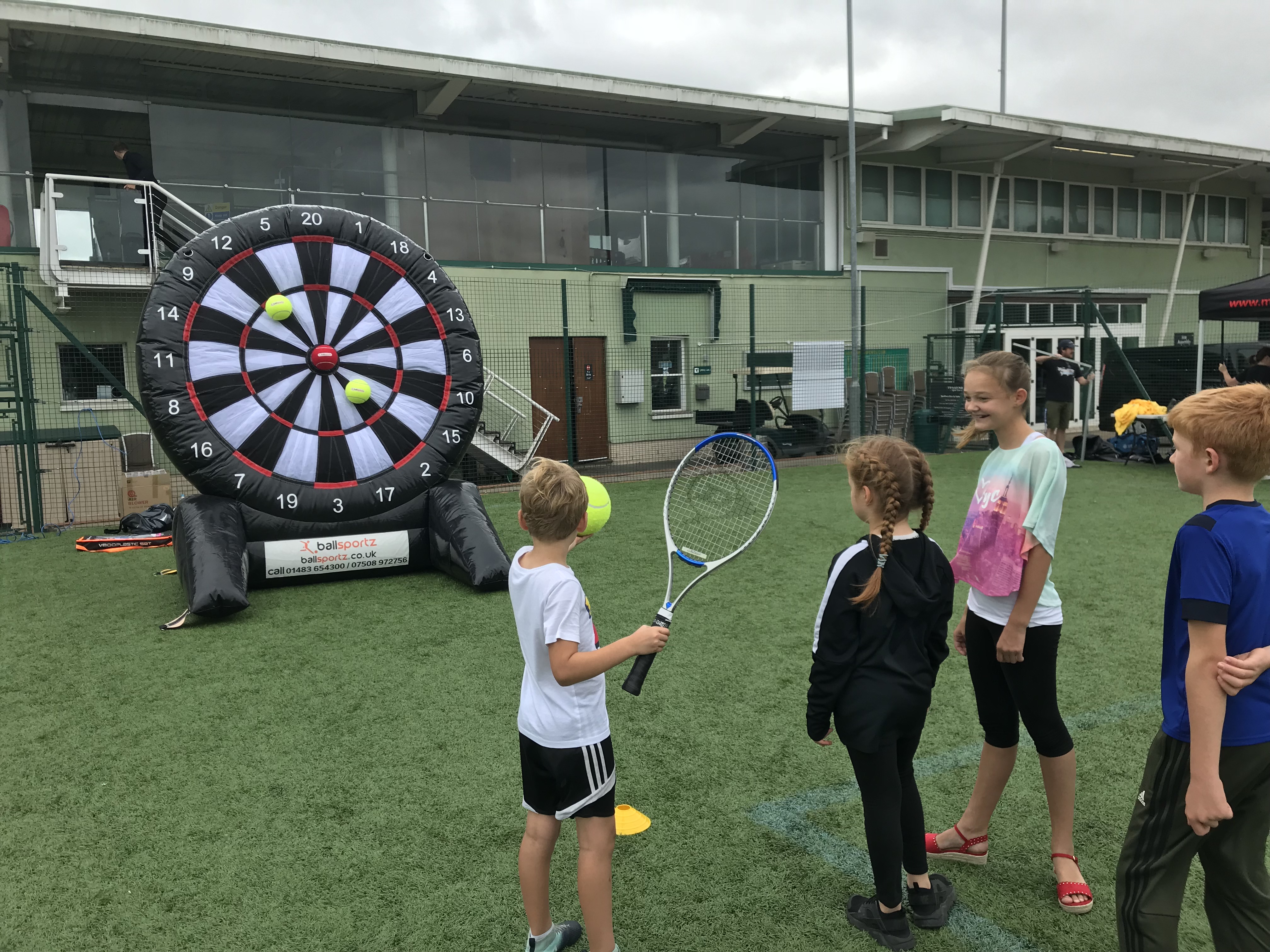 Children playing outdoor tennis target practice with a large inflatable dartboard.