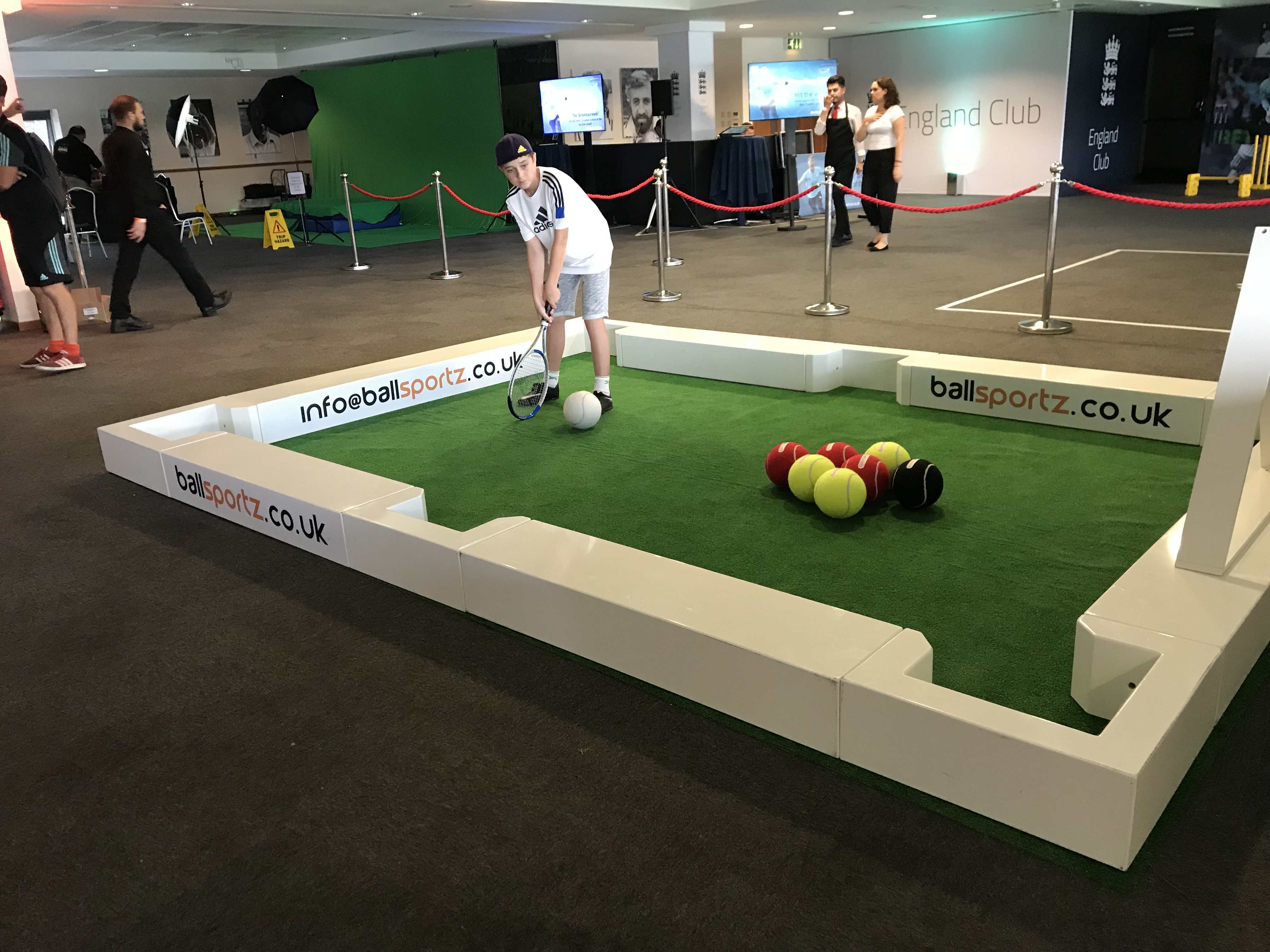 A person plays indoor mini-golf with soccer balls on a green mat.