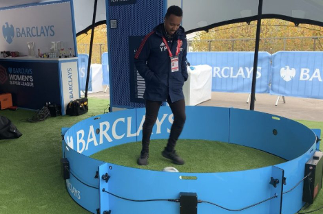 At a Barclays event, a man skillfully plays foot pool with a soccer ball in a small circular arena.