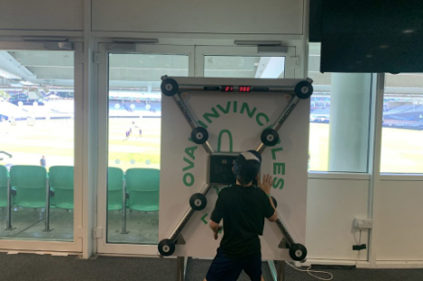A person wearing a cap engages with a reflex testing board in a room overlooking a foot pool and sports field.