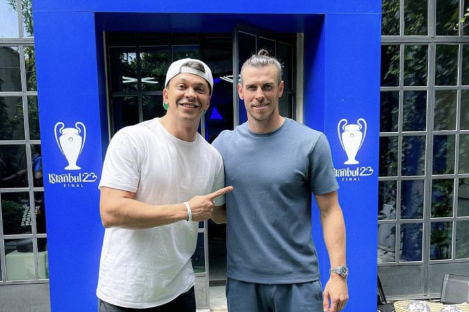 Two men stand in front of a blue Istanbul 2023 Champions League Final backdrop. The man on the left playfully points at the man on the right, as if challenging him to a game of foot pool.