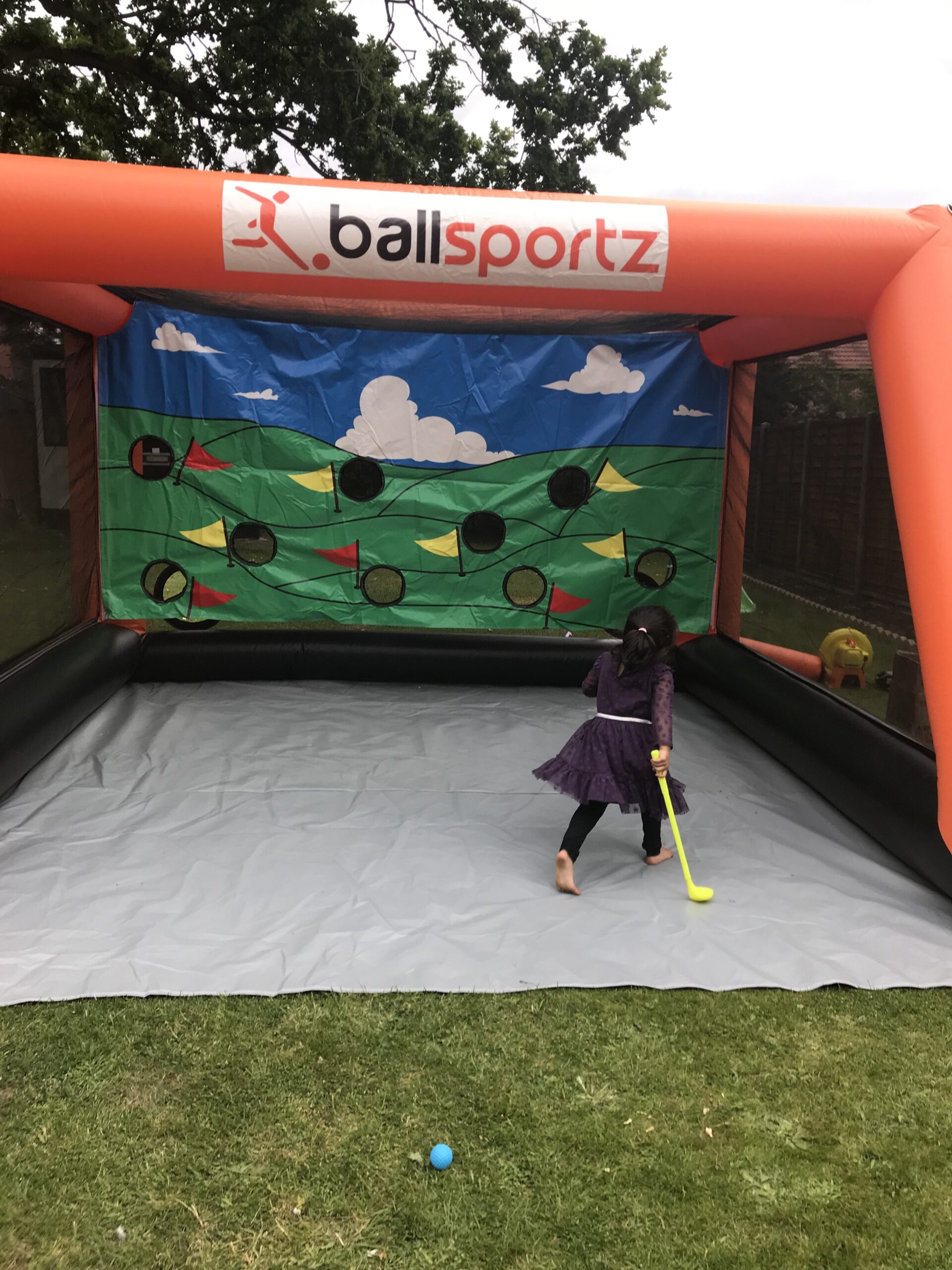 Child playing with a plastic hockey stick in an inflatable sports game setup with colorful targets.