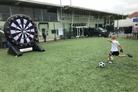 A child kicks a soccer ball with precision at a large inflatable dartboard target, mirroring the fun and strategy of foot pool on the sports field.