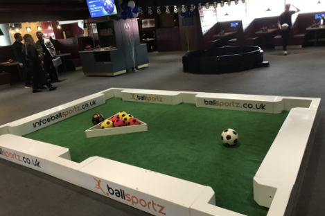 Experience the ultimate foot pool adventure in our indoor game area, featuring a giant pool table setup with large soccer balls on lush green turf. Surrounded by branded white barriers, it's the perfect blend of soccer and billiards fun!
