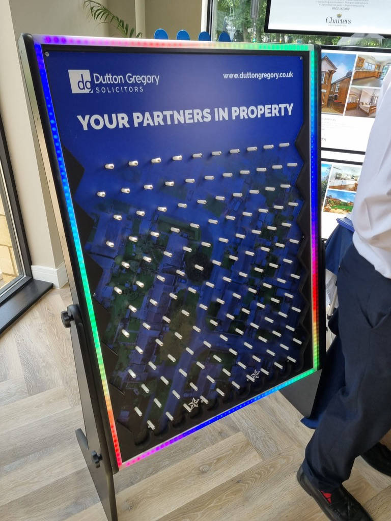A promotional display board with a colored frame titled "Your Partners in Property" from Dutton Gregory Solicitors, featuring a pegboard design reminiscent of Plink Game Hire—a playful twist on legal services.