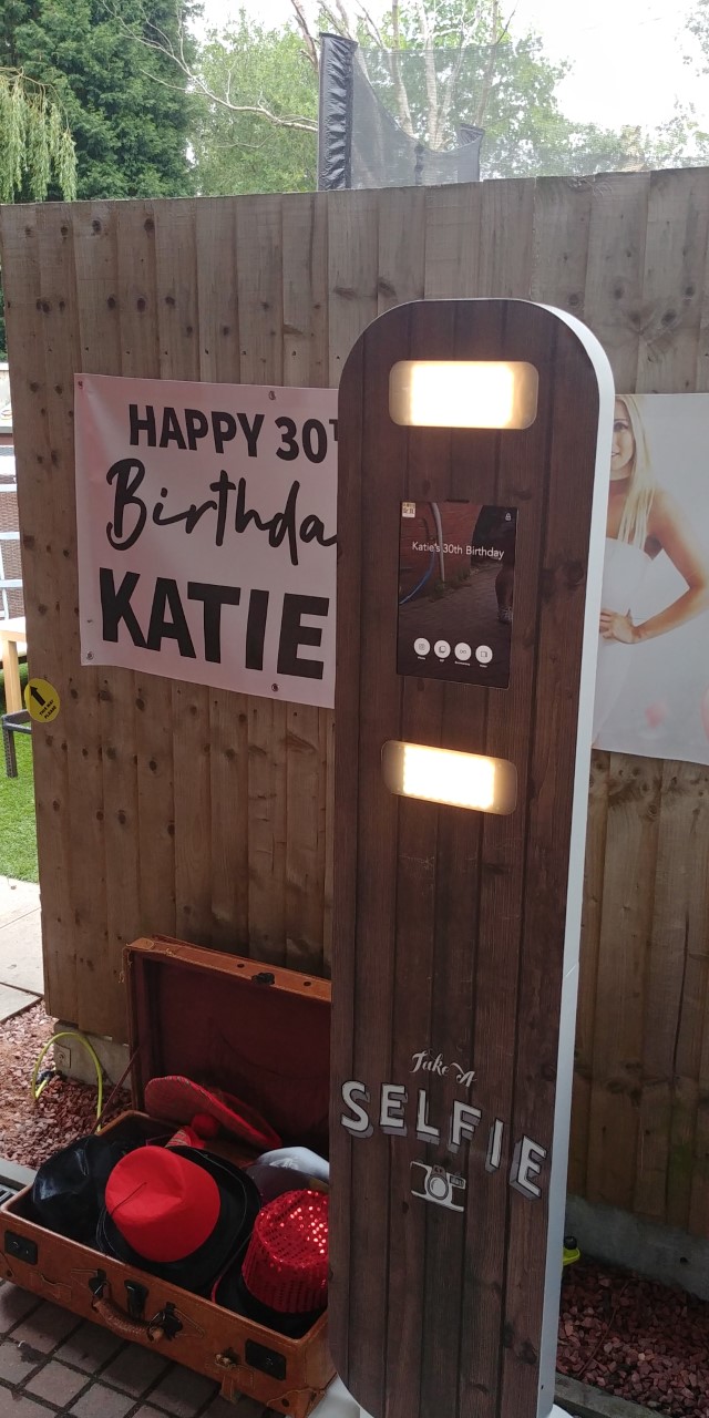 Photo booth hire setup with a "Happy 30th Birthday Katie" sign, surrounded by fun props in an inviting outdoor setting.