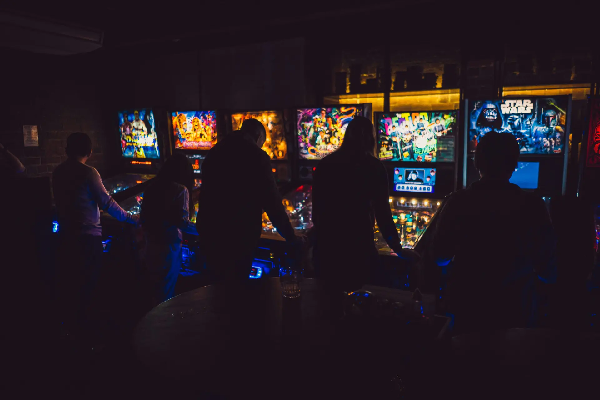 People enjoy pinball machines in a dim arcade—perfect for your next event with Arcade Games Hire.