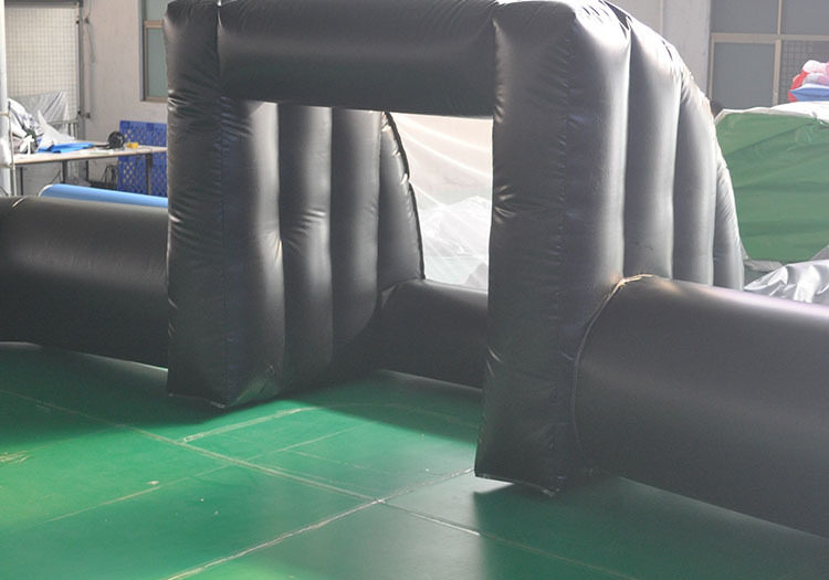 A large, black inflatable archway set on a green surface in an indoor space, with windows in the background.