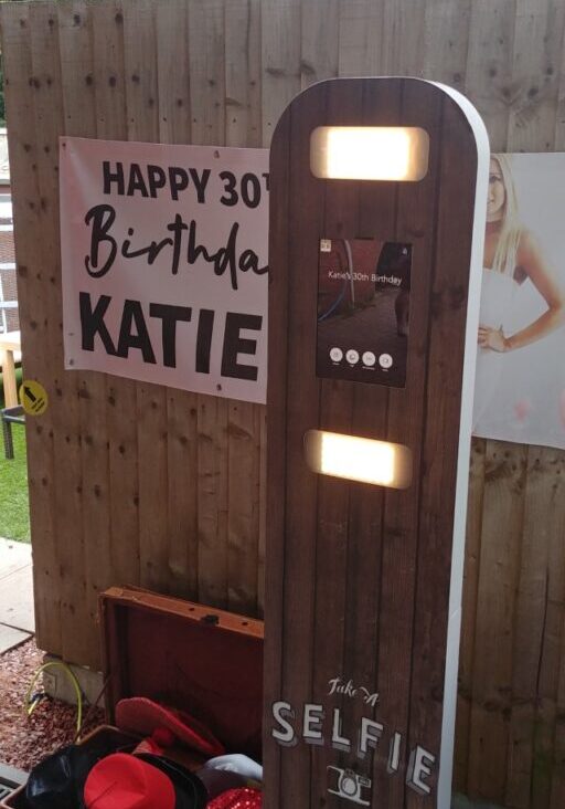 Photo booth hire setup with a "Happy 30th Birthday Katie" sign, surrounded by fun props in an inviting outdoor setting.