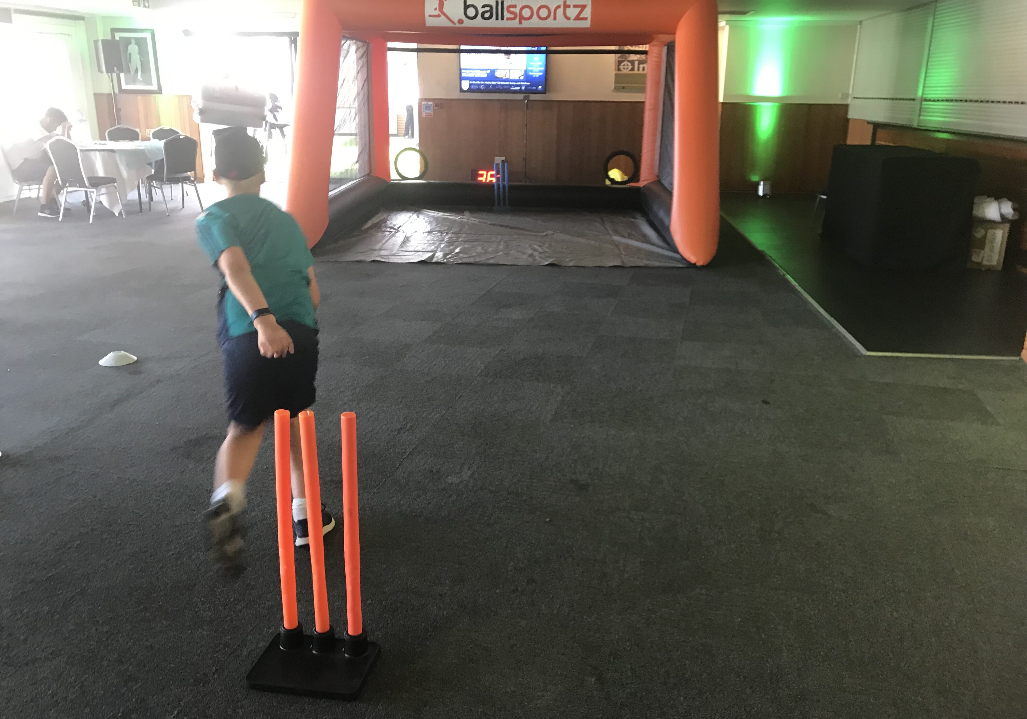 A person playing an indoor cricket game, aiming at an inflatable target with orange stumps in the foreground.